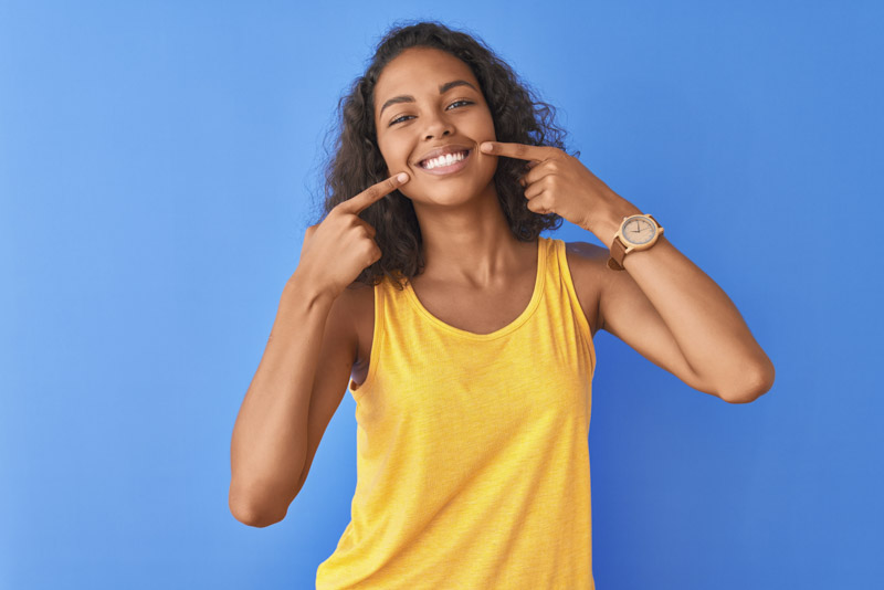 Woman in a yellow top pointing at her clear aligner