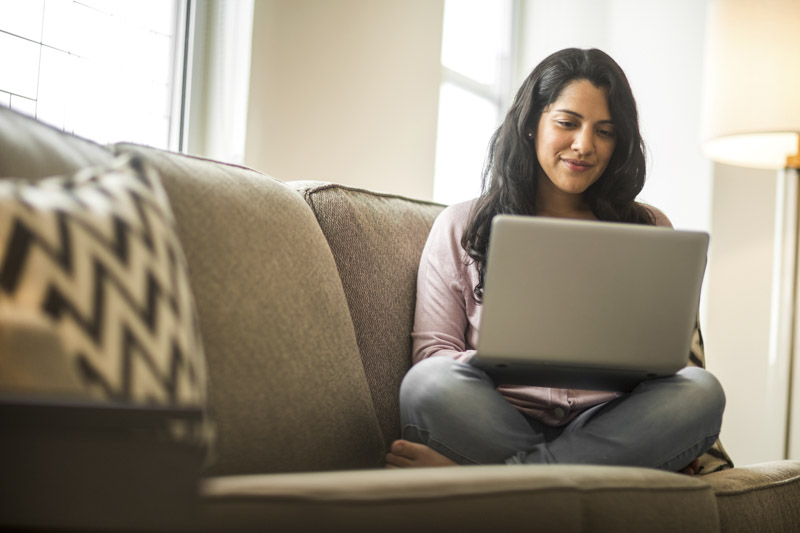 Young woman sitting on her couch while working on her laptop