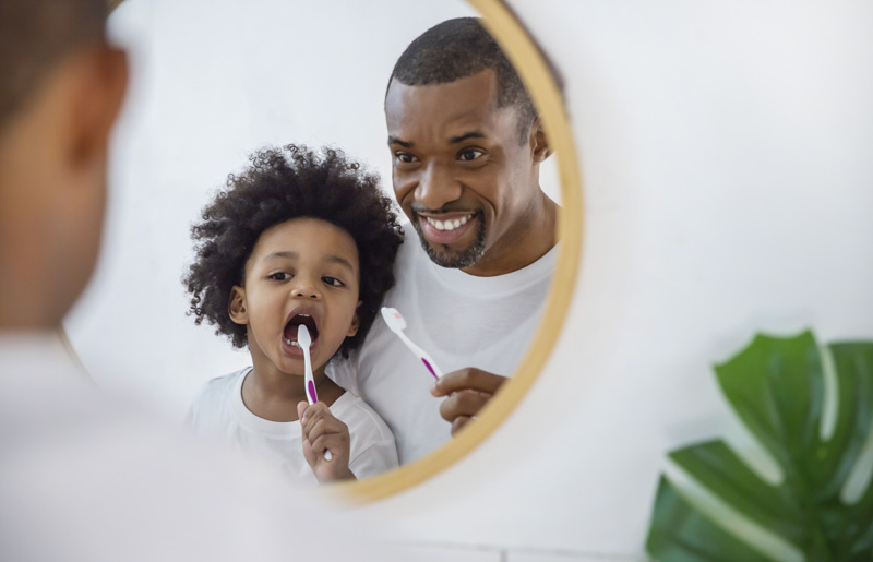 Father watching his child brush their teeth